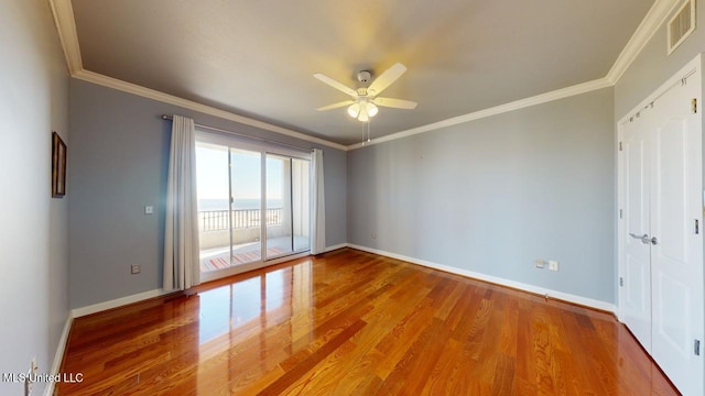 empty room featuring ceiling fan, crown molding, a water view, and hardwood / wood-style flooring