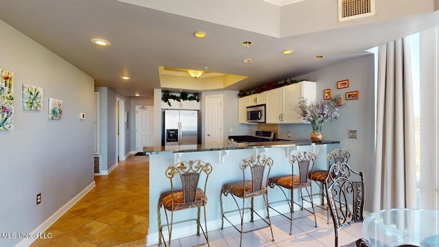 kitchen with kitchen peninsula, stainless steel appliances, a tray ceiling, white cabinets, and light tile patterned flooring