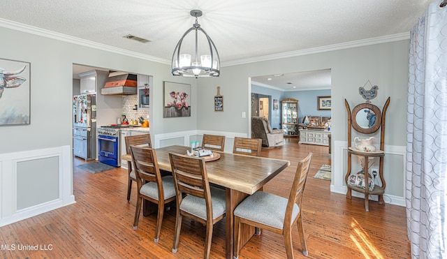 dining area featuring hardwood / wood-style floors, visible vents, a textured ceiling, crown molding, and a chandelier