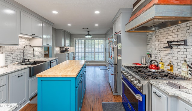 kitchen featuring dark wood-type flooring, premium range hood, butcher block counters, stainless steel appliances, and a sink