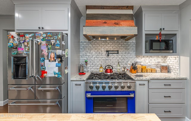 kitchen with light stone countertops, custom exhaust hood, appliances with stainless steel finishes, a textured ceiling, and backsplash