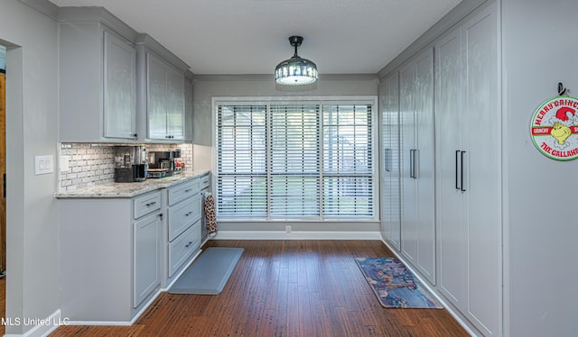 kitchen featuring light stone countertops, baseboards, gray cabinetry, dark wood-type flooring, and backsplash