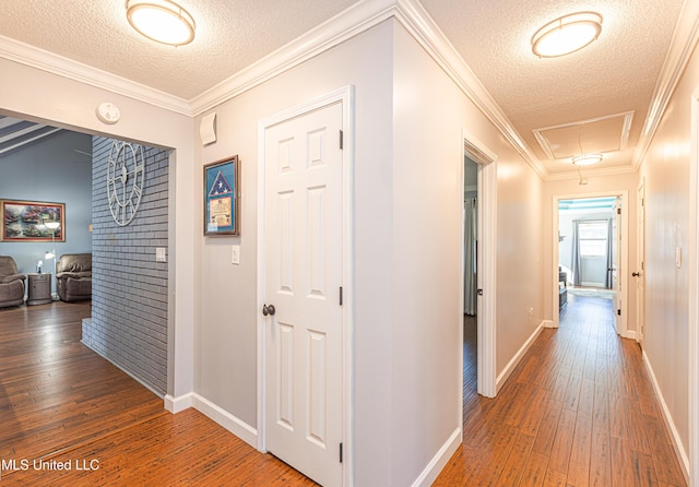 hall featuring baseboards, attic access, ornamental molding, a textured ceiling, and wood-type flooring