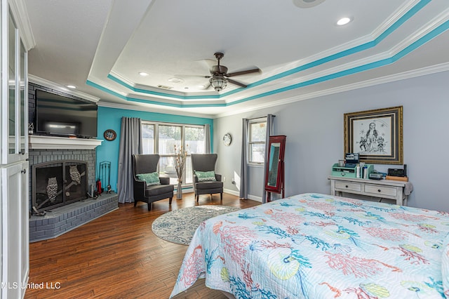 bedroom with ornamental molding, a tray ceiling, wood finished floors, a fireplace, and ceiling fan