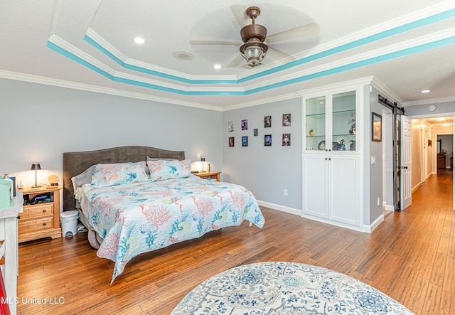 bedroom featuring a raised ceiling, a barn door, and wood finished floors