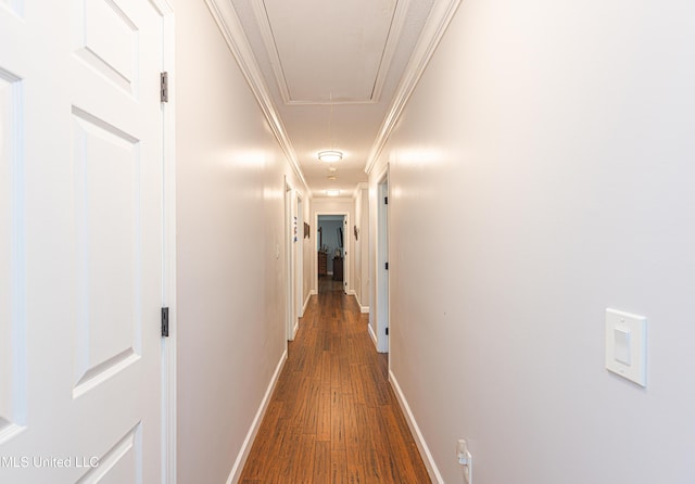 corridor featuring attic access, crown molding, dark wood-type flooring, and baseboards