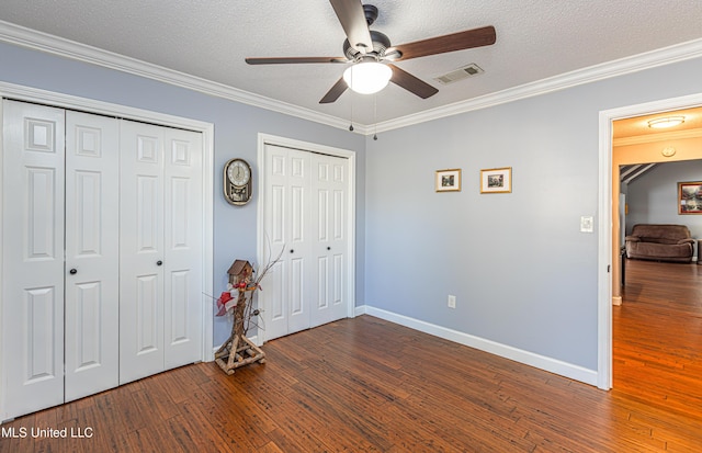 unfurnished bedroom with visible vents, two closets, a textured ceiling, wood-type flooring, and crown molding