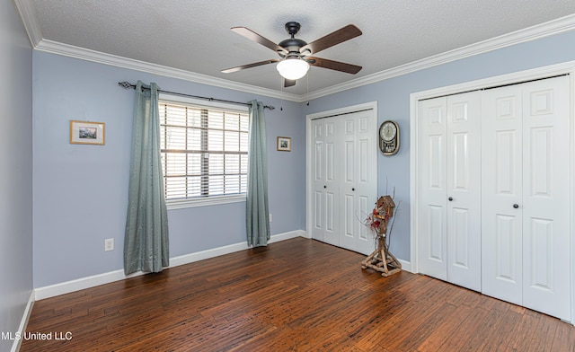 unfurnished bedroom with multiple closets, dark wood-type flooring, ornamental molding, and a textured ceiling