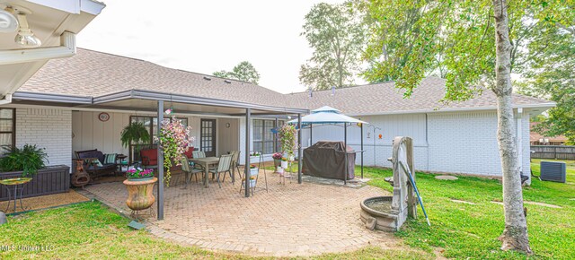 rear view of house featuring brick siding, a yard, a patio, and roof with shingles