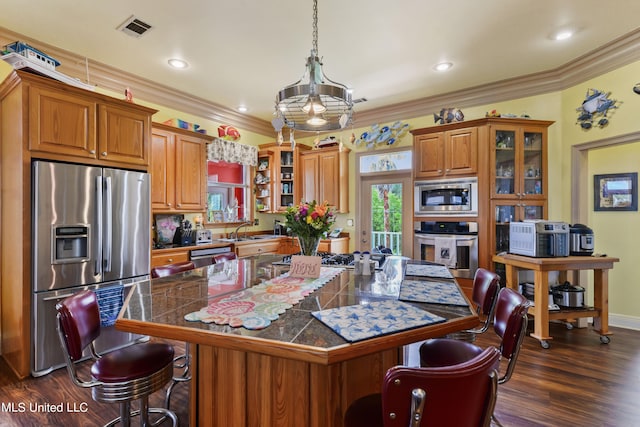 kitchen featuring hanging light fixtures, appliances with stainless steel finishes, a kitchen bar, dark wood-type flooring, and crown molding