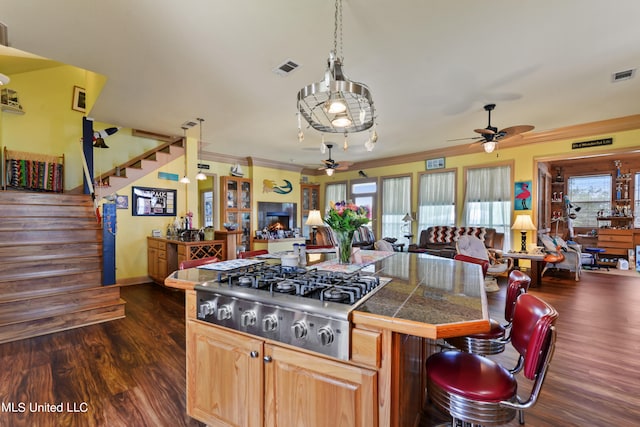 kitchen featuring ornamental molding, stainless steel gas stovetop, dark wood-type flooring, and a breakfast bar