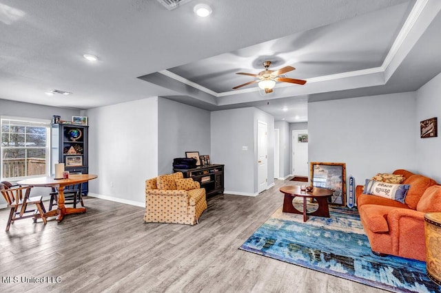 living room featuring a raised ceiling, crown molding, baseboards, and wood finished floors