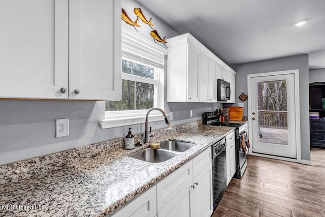 kitchen featuring light stone counters, dark wood-style flooring, a sink, white cabinets, and black appliances