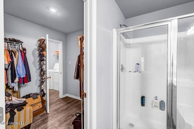 full bath featuring a stall shower, baseboards, a walk in closet, and wood finished floors