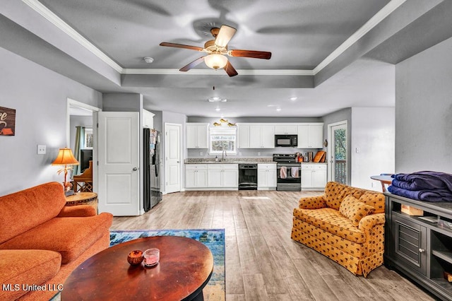 living area with light wood-type flooring, ornamental molding, a raised ceiling, and a ceiling fan