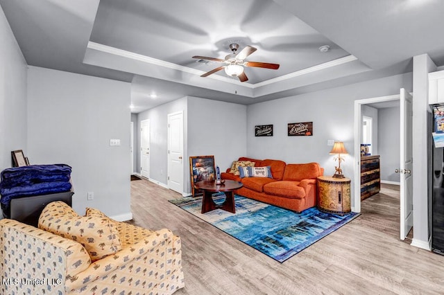 living room with light wood finished floors, ornamental molding, and a raised ceiling