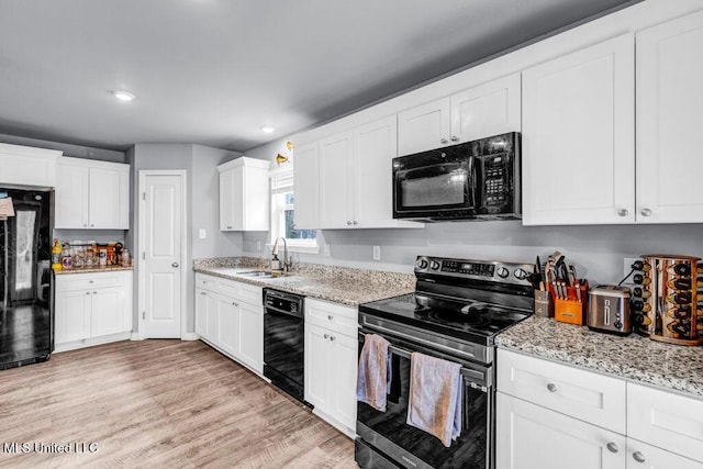 kitchen featuring white cabinets, light stone countertops, light wood-type flooring, black appliances, and a sink