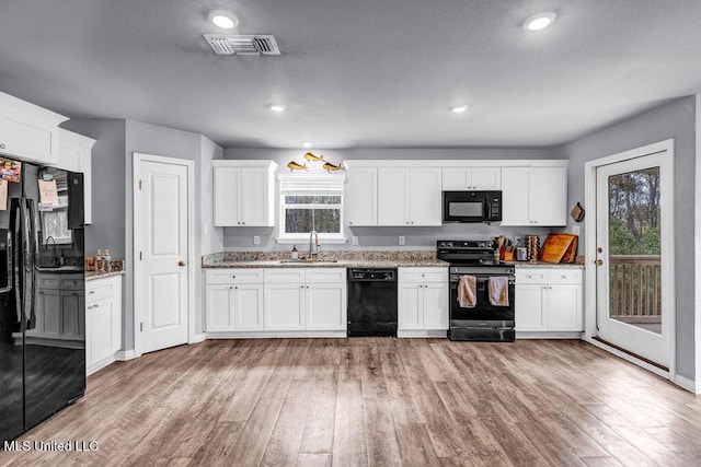 kitchen with a sink, visible vents, black appliances, light wood finished floors, and plenty of natural light