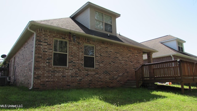 view of side of home with cooling unit, brick siding, a lawn, and a wooden deck