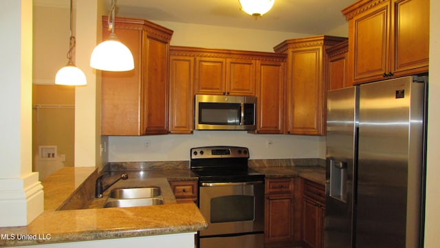 kitchen with stainless steel appliances, hanging light fixtures, brown cabinetry, a sink, and a peninsula