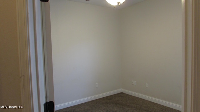 spare room featuring baseboards, dark colored carpet, and a ceiling fan