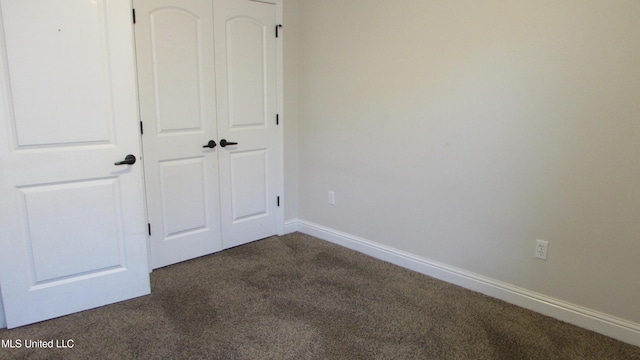 unfurnished bedroom with dark colored carpet, a closet, and baseboards