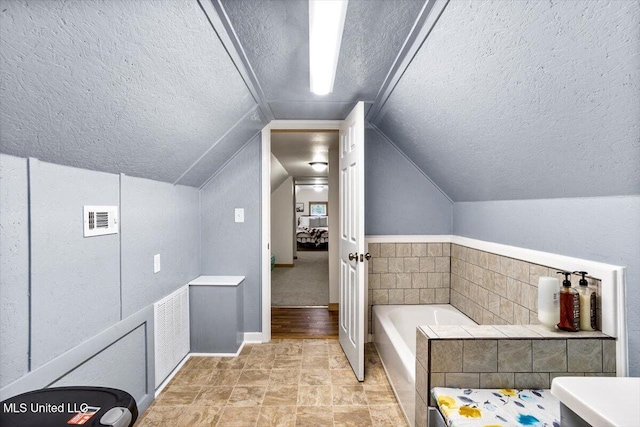 bathroom featuring a bathtub, vaulted ceiling, and a textured ceiling