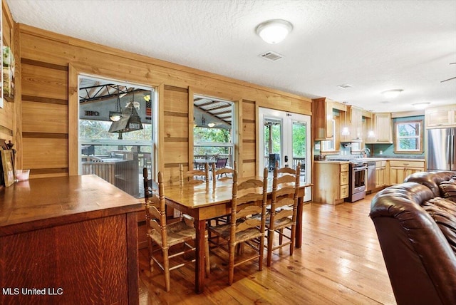 dining room with french doors, wood walls, a textured ceiling, sink, and light hardwood / wood-style flooring