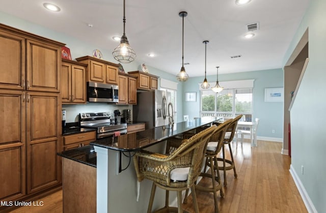 kitchen with a kitchen island with sink, stainless steel appliances, a breakfast bar, pendant lighting, and light hardwood / wood-style floors