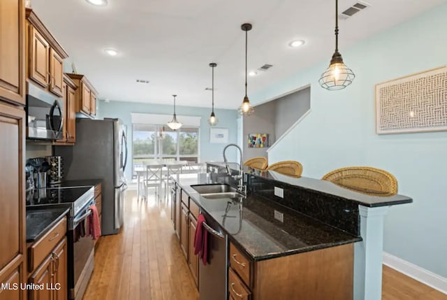 kitchen with appliances with stainless steel finishes, a center island with sink, decorative light fixtures, and sink