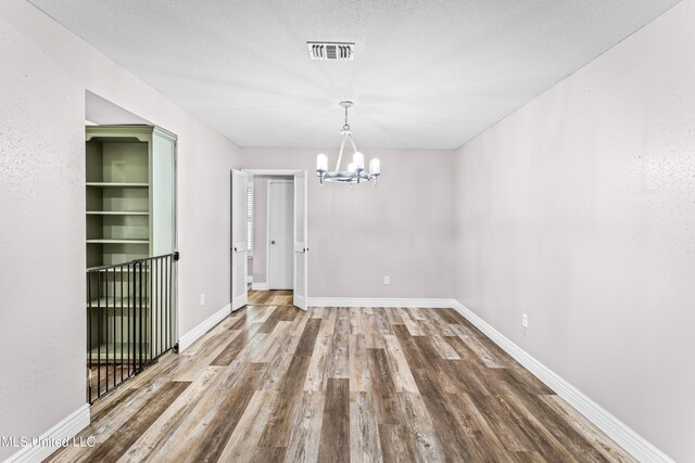 unfurnished dining area featuring baseboards, visible vents, wood finished floors, and a chandelier