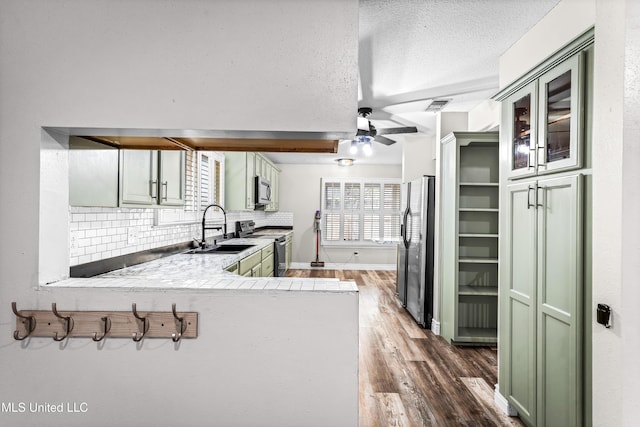 kitchen featuring a sink, green cabinets, tasteful backsplash, a textured ceiling, and stainless steel appliances