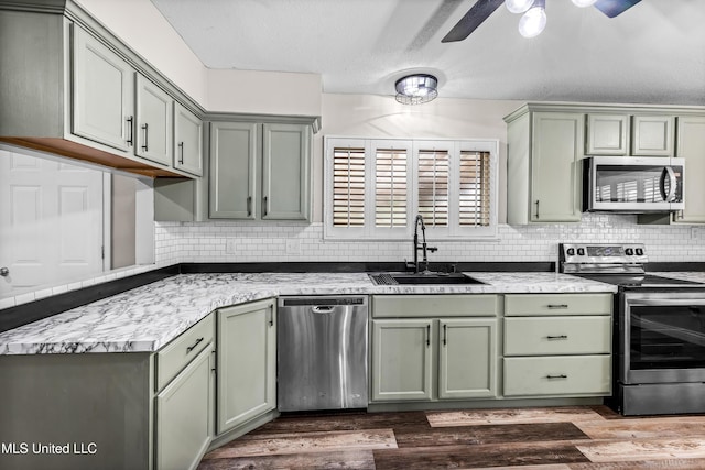 kitchen featuring ceiling fan, appliances with stainless steel finishes, a sink, green cabinetry, and dark wood-style floors