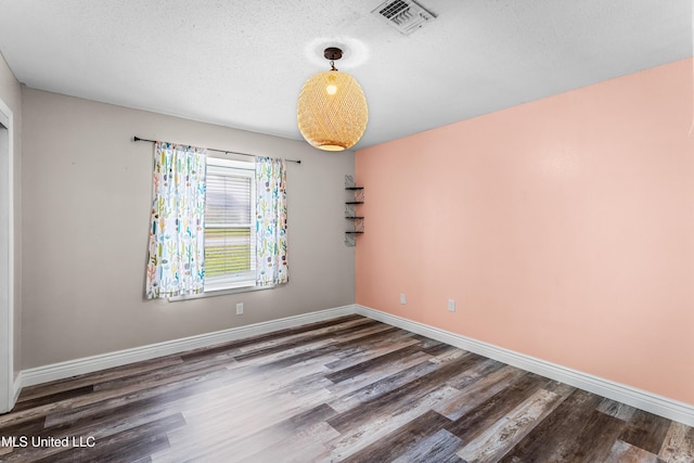 spare room with baseboards, visible vents, wood finished floors, and a textured ceiling