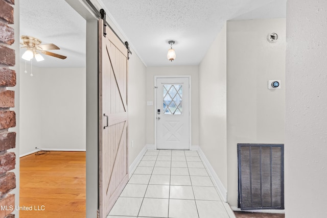 doorway to outside featuring a barn door, a textured ceiling, light tile patterned floors, visible vents, and ceiling fan
