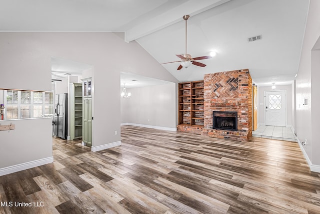 unfurnished living room featuring visible vents, wood finished floors, ceiling fan with notable chandelier, and a brick fireplace