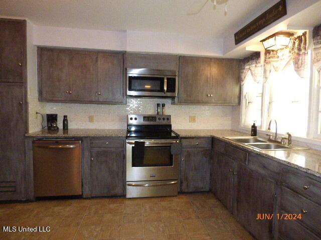 kitchen with light stone countertops, tasteful backsplash, appliances with stainless steel finishes, dark brown cabinets, and sink