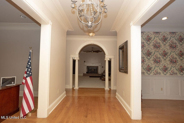 hallway with an inviting chandelier, light hardwood / wood-style flooring, crown molding, and decorative columns