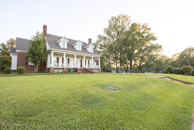 cape cod house with covered porch, a front lawn, and a chimney