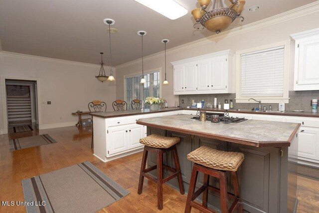 kitchen featuring a peninsula, a sink, white cabinetry, dark wood-style flooring, and ornamental molding