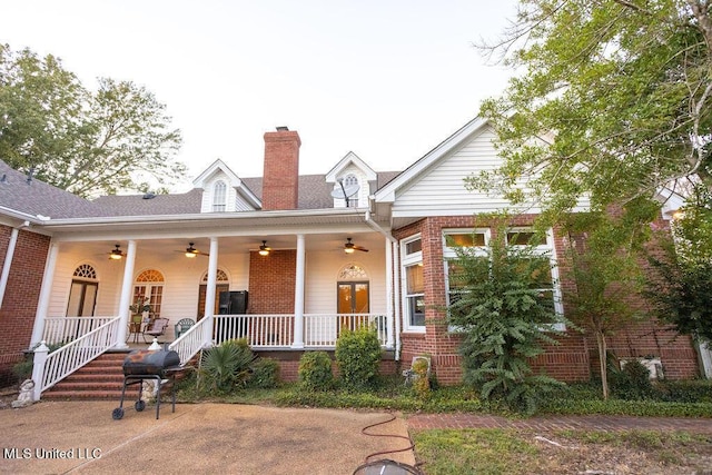 view of front facade with a ceiling fan, a chimney, a porch, and brick siding