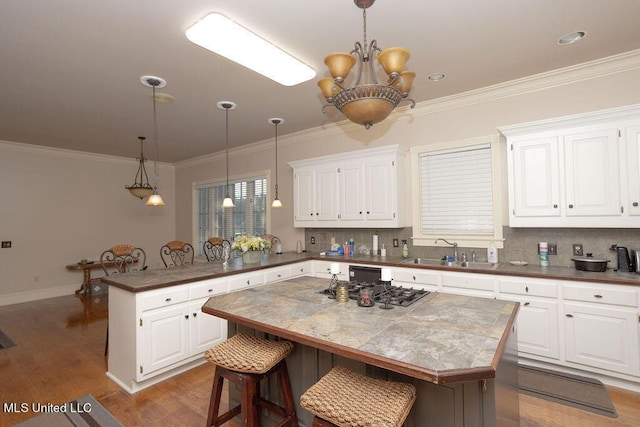 kitchen with a sink, a peninsula, a chandelier, wood finished floors, and white cabinetry