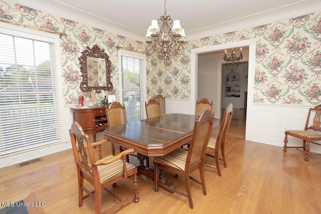 dining area featuring a chandelier, wallpapered walls, wainscoting, crown molding, and light wood-type flooring