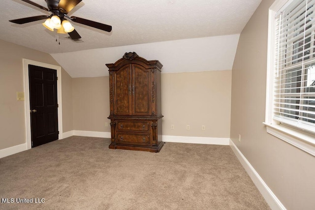 carpeted spare room with vaulted ceiling, a ceiling fan, baseboards, and a textured ceiling