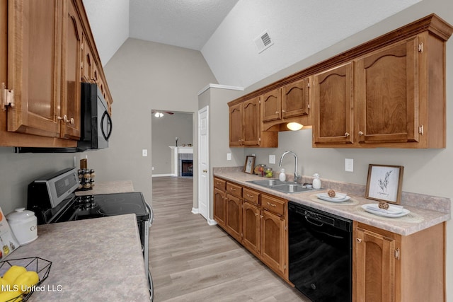 kitchen featuring sink, a tile fireplace, black appliances, light hardwood / wood-style floors, and lofted ceiling