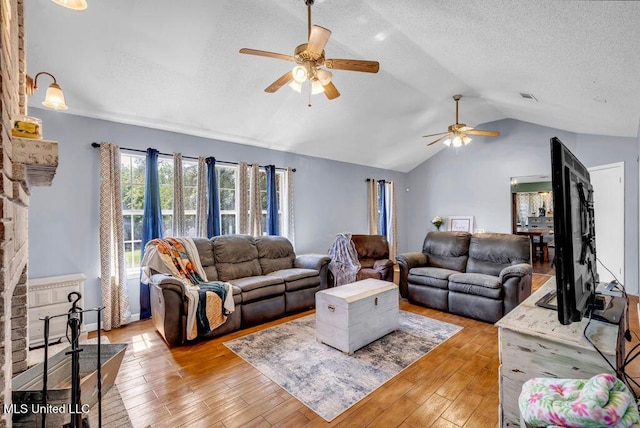 living area featuring ceiling fan, a textured ceiling, visible vents, vaulted ceiling, and light wood finished floors
