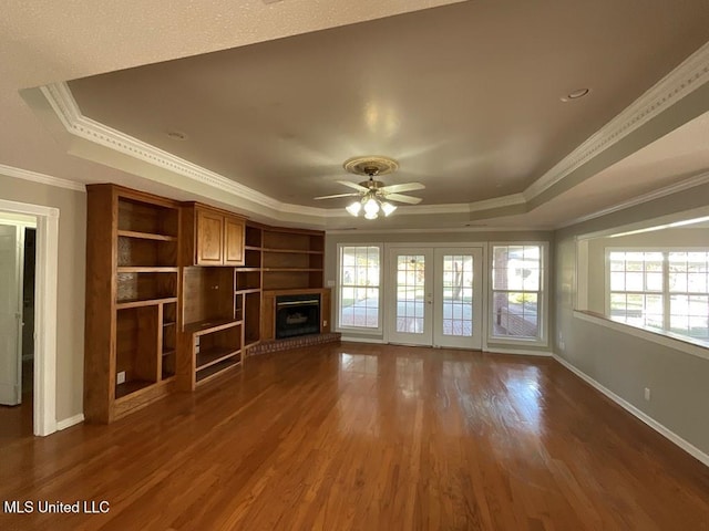 unfurnished living room featuring a tray ceiling, ceiling fan, dark hardwood / wood-style floors, and ornamental molding