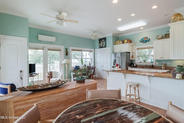 kitchen with a wall mounted AC, kitchen peninsula, stainless steel fridge, white cabinetry, and light tile patterned flooring