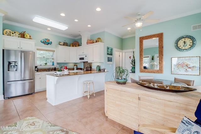 kitchen featuring light tile patterned floors, stainless steel refrigerator with ice dispenser, a kitchen bar, crown molding, and white cabinetry