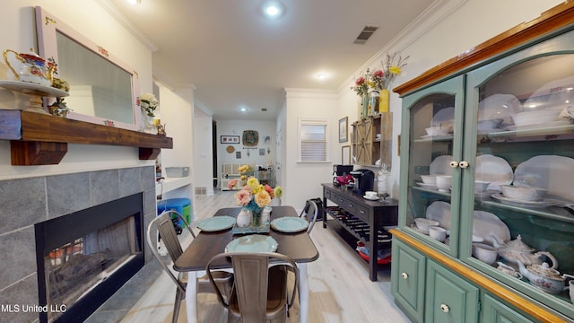 dining room featuring crown molding, visible vents, recessed lighting, light wood-type flooring, and a tile fireplace
